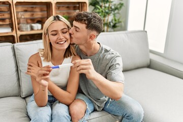 Poster - Young caucasian couple smiling happy holding pregnacy test at home.