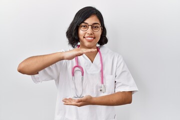 Poster - Young hispanic doctor woman wearing stethoscope over isolated background gesturing with hands showing big and large size sign, measure symbol. smiling looking at the camera. measuring concept.