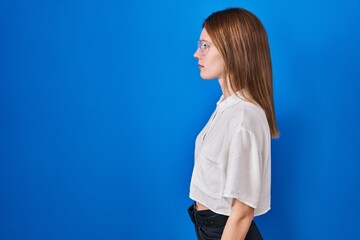 Poster - Beautiful woman standing over blue background looking to side, relax profile pose with natural face with confident smile.