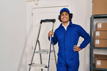 Wall Mural - Young hispanic man technician holding ladder standing at office
