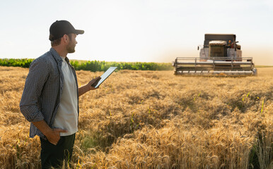 Fototapete - Farmer with digital tablet on a background of combine harvester. Smart farming concept.