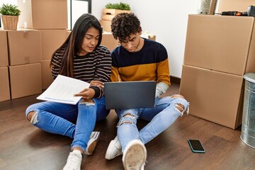 Poster - Young latin couple with serious expression using laptop sitting on the floor at new home.