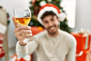 Poster - Young hispanic man smiling happy wearing christmas hat drinking champagne at home.