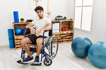 Sticker - Hispanic man sitting on wheelchair at physiotherapy clinic making fish face with lips, crazy and comical gesture. funny expression.