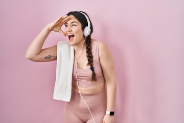 Sticker - Young brunette woman wearing sportswear and headphones very happy and smiling looking far away with hand over head. searching concept.