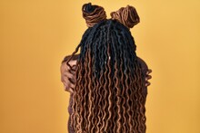 African Woman With Braided Hair Standing Over Yellow Background Hugging Oneself Happy And Positive From Backwards. Self Love And Self Care