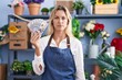 © Krakenimages.com - Young blonde woman working at florist shop holding dollars thinking attitude and sober expression looking self confident