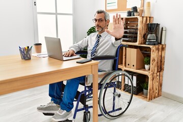 Canvas Print - Middle age hispanic man working at the office sitting on wheelchair doing stop sing with palm of the hand. warning expression with negative and serious gesture on the face.