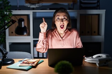 Canvas Print - Middle age hispanic woman working using computer laptop late at night pointing finger up with successful idea. exited and happy. number one.