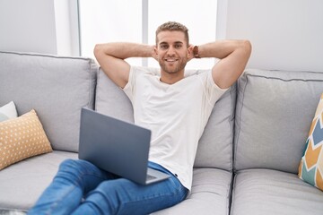 Canvas Print - Young caucasian man using laptop relaxed with hands on head at home