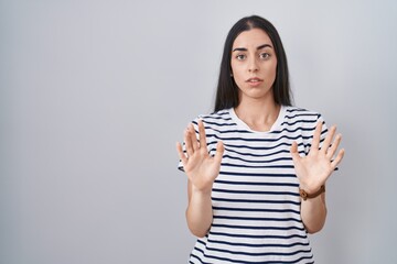 Sticker - Young brunette woman wearing striped t shirt moving away hands palms showing refusal and denial with afraid and disgusting expression. stop and forbidden.