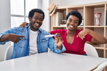 Canvas Print - Young african american couple holding pregnancy test result pointing finger to one self smiling happy and proud