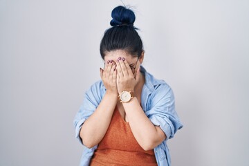 Sticker - Young modern girl with blue hair standing over white background with sad expression covering face with hands while crying. depression concept.