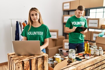 Sticker - Young woman and man wearing volunteer t shirt at donations stand thinking attitude and sober expression looking self confident