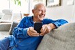 © Krakenimages.com - Senior man with grey hair sitting on the sofa at the living room of his house using smartphone
