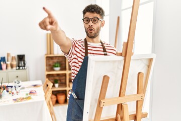 Poster - Arab young man at art studio pointing with finger surprised ahead, open mouth amazed expression, something on the front