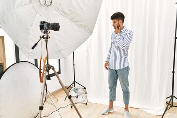 Sticker - Arab young man posing as model at photography studio pointing to the eye watching you gesture, suspicious expression