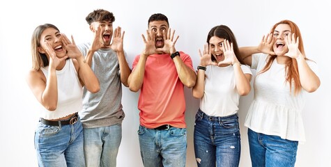 Wall Mural - Group of young friends standing together over isolated background smiling cheerful playing peek a boo with hands showing face. surprised and exited