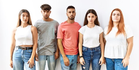 Wall Mural - Group of young friends standing together over isolated background relaxed with serious expression on face. simple and natural looking at the camera.