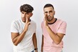 © Krakenimages.com - Young gay couple standing over isolated background hand on mouth telling secret rumor, whispering malicious talk conversation