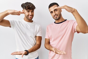 Poster - Young gay couple standing over isolated background gesturing with hands showing big and large size sign, measure symbol. smiling looking at the camera. measuring concept.