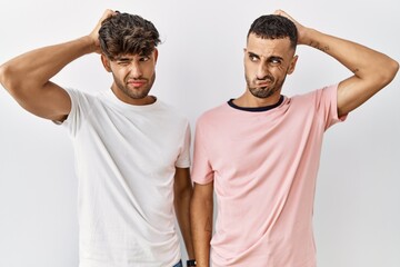 Wall Mural - Young gay couple standing over isolated background confuse and wondering about question. uncertain with doubt, thinking with hand on head. pensive concept.