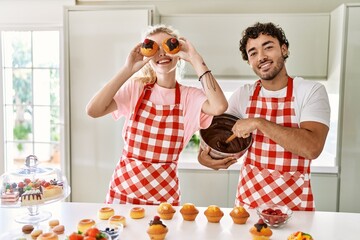 Young couple smiling happy cooking sweets holding pumpkin on eyes at kitchen.