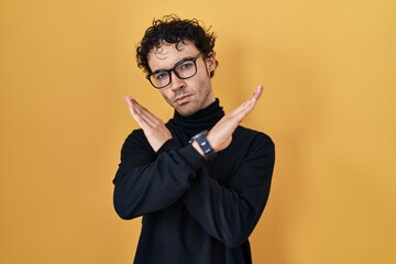 Poster - Hispanic man standing over yellow background rejection expression crossing arms doing negative sign, angry face