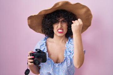 Sticker - Young brunette woman with curly hair using reflex camera annoyed and frustrated shouting with anger, yelling crazy with anger and hand raised