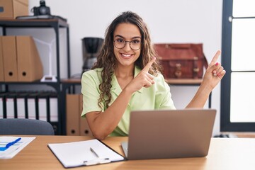 Sticker - Young hispanic woman working at the office wearing glasses smiling and looking at the camera pointing with two hands and fingers to the side.