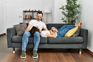 Sticker - Middle age hispanic couple relaxed sitting on the sofa with dog at home.