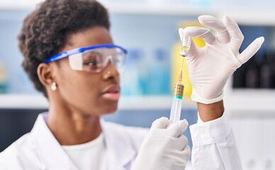 Wall Mural - African american woman wearing scientist uniform holding vaccine at laboratory