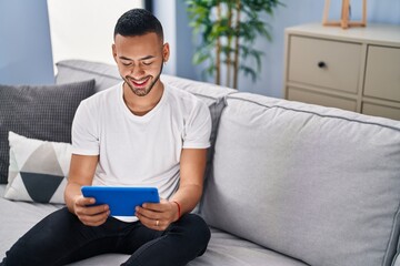 Canvas Print - African american man using touchpad sitting on sofa at home