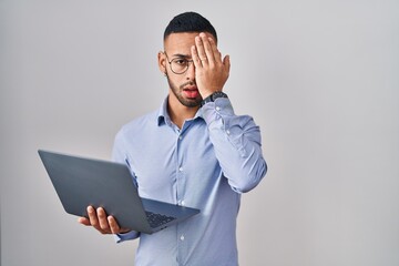 Poster - Young hispanic man working using computer laptop yawning tired covering half face, eye and mouth with hand. face hurts in pain.