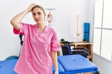 Young blonde woman working at pain recovery clinic confuse and wonder about question. uncertain with doubt, thinking with hand on head. pensive concept.