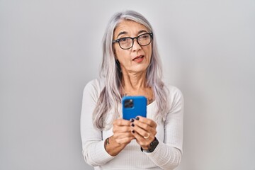 Sticker - Middle age woman with grey hair using smartphone typing message winking looking at the camera with sexy expression, cheerful and happy face.