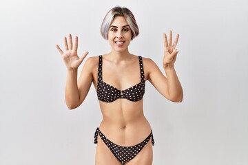 Canvas Print - Young beautiful woman wearing swimsuit over isolated background showing and pointing up with fingers number eight while smiling confident and happy.