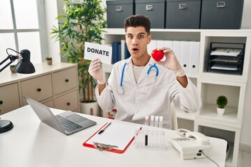 Wall Mural - Young hispanic doctor man supporting organs donations afraid and shocked with surprise and amazed expression, fear and excited face.