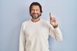 © Krakenimages.com - Handsome middle age man wearing casual sweater over blue background showing and pointing up with finger number one while smiling confident and happy.