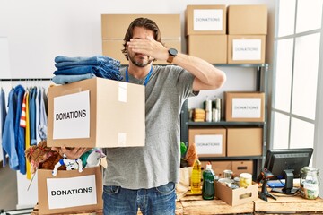 Poster - Handsome middle age man holding donations box for charity at volunteer stand covering eyes with hand, looking serious and sad. sightless, hiding and rejection concept