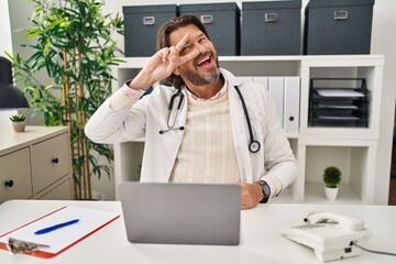 Sticker - Handsome middle age doctor man working at the clinic doing peace symbol with fingers over face, smiling cheerful showing victory