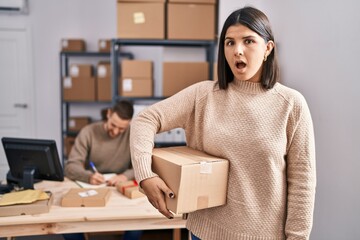 Two young people working at small business ecommerce scared and amazed with open mouth for surprise, disbelief face