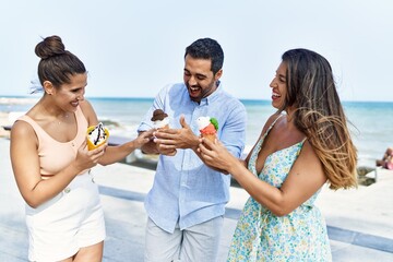 Sticker - Three young hispanic friends smiling happy eating ice cream at the beach.