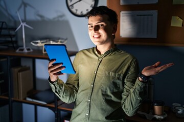 Wall Mural - Non binary person using touchpad device at night pointing aside with hands open palms showing copy space, presenting advertisement smiling excited happy