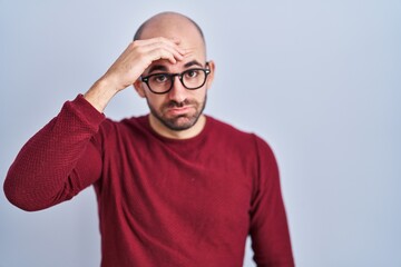 Sticker - Young bald man with beard standing over white background wearing glasses worried and stressed about a problem with hand on forehead, nervous and anxious for crisis