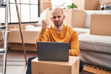 Canvas Print - Young bald man with beard moving to a new house using laptop annoyed and frustrated shouting with anger, yelling crazy with anger and hand raised