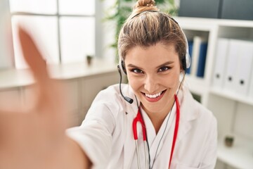 Poster - Young blonde woman wearing doctor uniform make selfie by the camera at clinic