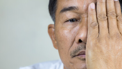 Close-up of a senior man's eyes looking at the camera and a hand covering one eye