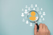 © Dilok - Hand holding magnifier glass with yellow person icon among white people icons for Customer focus group ,recruitment and human development concept.