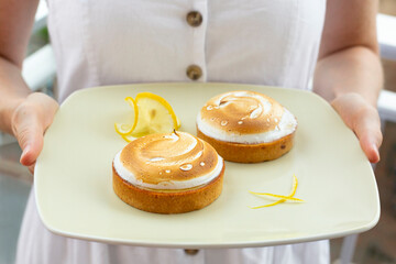 Sticker - Woman holding a plate with lemon meringue mini tarts. Shortbread crust, lemon curd filling.